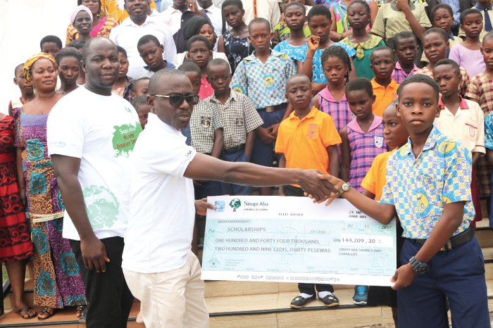Mr Vincent Amponsah (left), Head of Business, Sinapi Aba Savings and Loans, handing over a dummy cheque for GH¢ 144,209 to one of the beneficiaries on behalf of the 218 recipients. At the extreme left is Mr Eric Ofoe-Barnor, the Head of Marketing & Deposits of Sinapi Aba