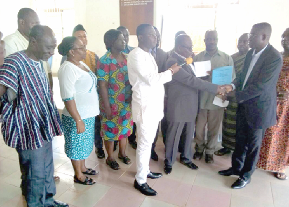 Mr William Bediako Asante (right), the DCE,  receiving the report from Dr Kofi Afoakwa while other members of the committee look on