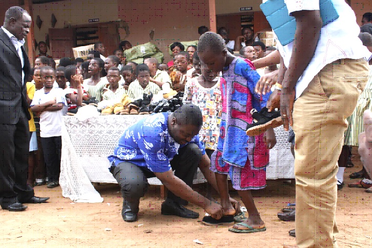The Country Director of Compassion International Ghana, Padmore Baffour Agyapong, assisting a child to put on his new shoes.