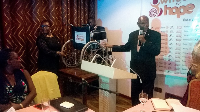 Mr Okudzeto (with mic) pointing at one of the wheelchairs after the unveiling ceremony, while the Club Vice President, Ms Gifty Annan-Myers, looks on