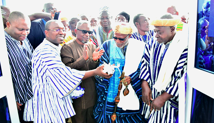Mr John Kweku Asamoah (MD/CEO) being assisted by Zohi Naa, Salifu Mahmud, a representative of the Overlord of the Dagbon Traditional Area, to cut the tape to open the branch
