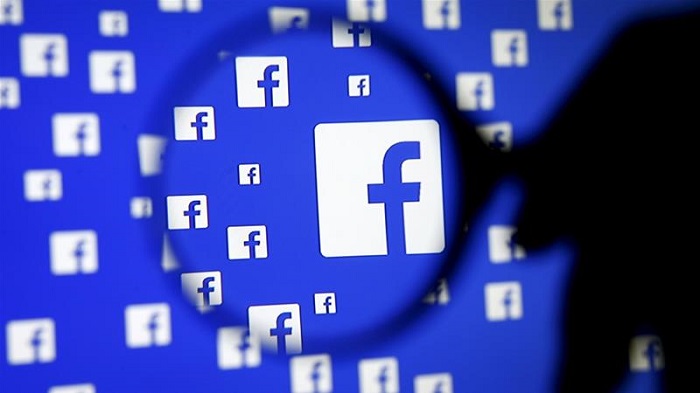 A man poses with a magnifier in front of a Facebook logo on display [Dado Ruvic/Reuters]