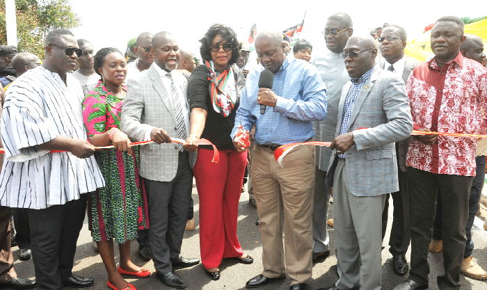 President Mahama being assisted by some government officials to cut the tape to inaugurate the road