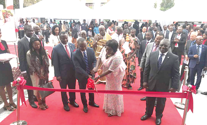 Mrs Freda Prempeh (right) being assisted to cut the tape to formally open the new bank.