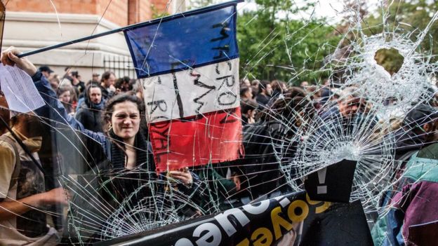 A protester holds the French Tricolour with an anti-Macron slogan outside a destroyed McDonald's