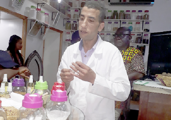 A  traditional herbalist explains to journalists the uses of various herbs, oils  and spices in  his shop
