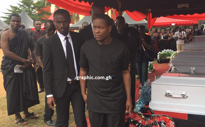 Pastor Ato Kessie (in all black attire) being escorted by a friend after laying wreaths on the coffin of the wife and four others at the funeral grounds 