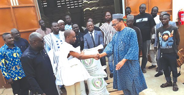 Mr Sekou Sangare (right) presenting a bag of the cereals to Dr Sagre Bambangi, while Alhaji Hanan Abdul-Wahab (left), the CEO of NAFCO and some officials from ECOWAS and NAFCO look on