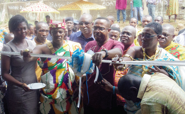 Mr Kwamena Duncan (middle), the Central Regional Minister being assisted by Osabarima Bishop Boappiah Afriyie II (left) to cut the tape to inaugurate the new market 