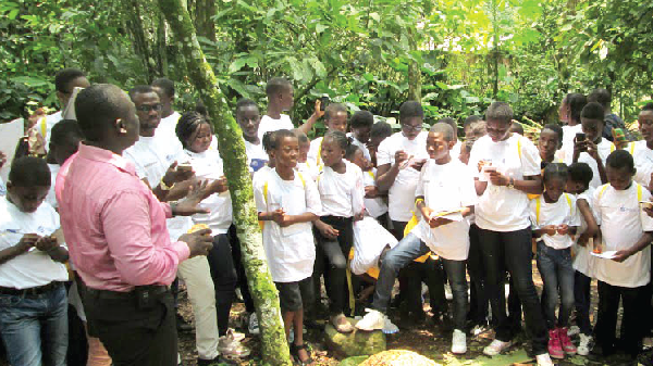Mr Lloyd Brobbey Adasi, Public Affairs Officer, CRIG, explaining to the pupils the cocoa planting and harvesting processes at the Tetteh Quarshie Cocoa Farm at Mampong in the