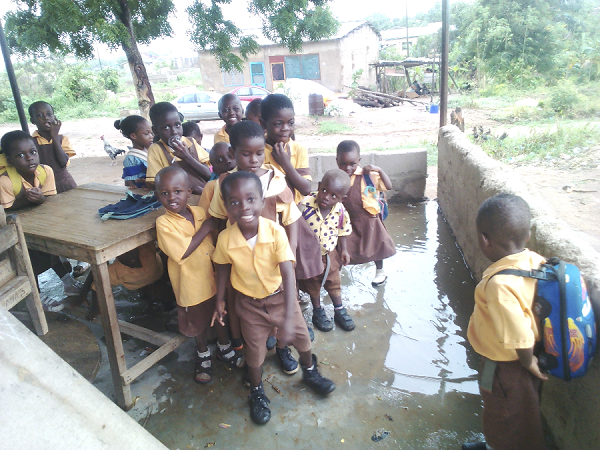 The pupils standing in the wet makeshift classroom  after a rainfall.