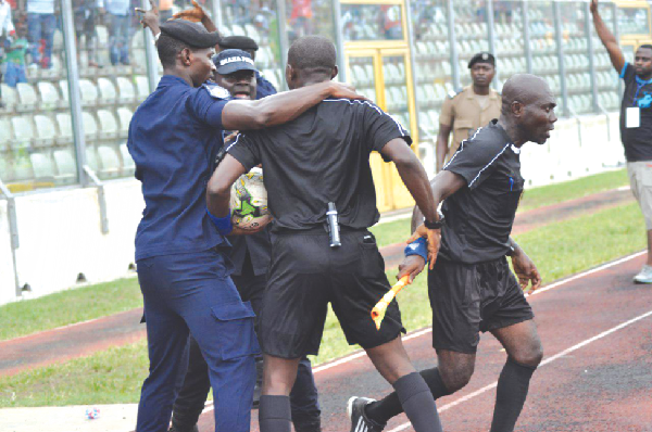 Police personnel shielding the visibly terrified referees to safety after being pelted by some irate Kotoko supporters at halftime. Picture: Emmanuel Baah