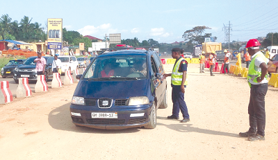 A policeman confronting a driver for illegally using the refilled median of the ongoing Pokuase interchange project as the engineer looks on