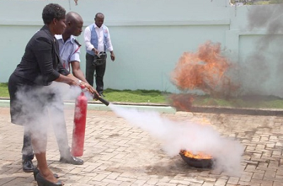 Mr Micheal Obimpeh, the Assistant Station Officer, assisting Ms Philomena Woolly, the Deputy Registrar, Nursing and Midwifery Council, to quench fire in a demonstration