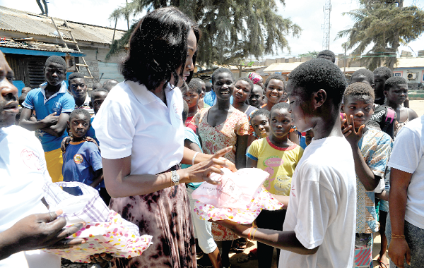 Miss Sheila Azuntaba presenting some books to one of the children while others wait for their turn 