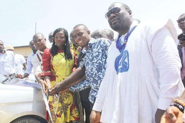 Ms Seyram Alhassan (arrowed) being assisted by NPP officials to cut the tape to inaugurate the Ayawaso West Wuogon Entrepreneurial Scheme. INSET: The cars. Picture: Maxwell Ocloo