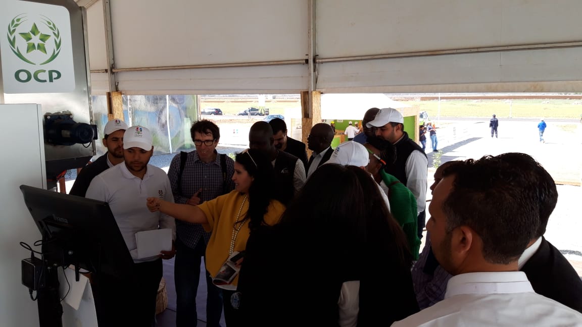 Madam Fatiha Charradi ( In yellow, with hand raised ) with other staff of OCP and farmers , demonstrating the blending of fertilisers during the visit