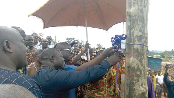 Mr Raymond Nana Damptey (left) and Mr Owuraku Aidoo (in spectacles) supporting Mr John Osei Frimpong (right) to switch on the light at Abohema. Looking on are Nana Amanie Ankrah and some residents of the community. 