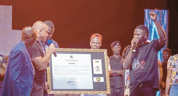 Mr Wahala Hakeem (2nd left), the Chief Executive of Wahala Entertainment, handing a citiation to Stonebwoy (right). With them is Mr Ashim Morton (left)