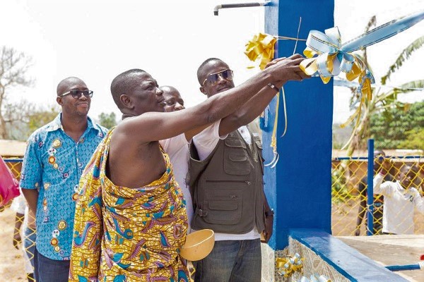 Mr Kwaku Tweneboah Ofosu (right) being assisted by Abusuapanyin Ofori (in cloth), chief of Asasekorkor, to cut the tape to inaugurate the mechanised borehole. Looking on is Mr Carlos Arko (extreme left), the project manager