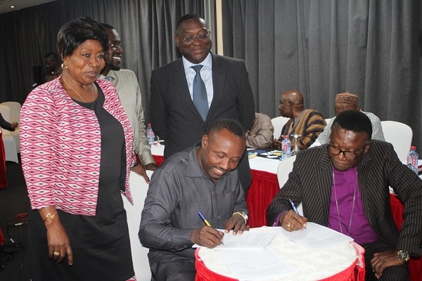 Rev. Professor Emmanuel Asante (right) and Mr John Boadu (seated 2nd right) signing the document at the meeting in Accra. Those looking on include Ms Rita Asobayire (left) and Mr Yaw Buaben Asamoah (standing 3rd left), both officials of the NPP. Picture: Gabriel Ahiabor