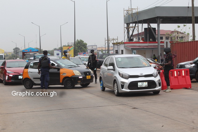 A taxicab being shepherded off the road to return home by armed policemen during the partial lockdown imposed on Accra