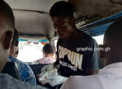 A commercial bus conductor (trotro mate) using gloves to handle money on a commute from La to Tema Station (Accra)