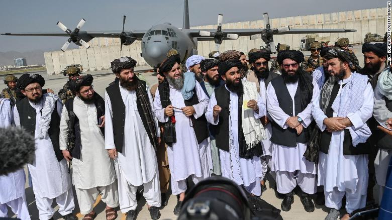 Taliban spokesman Zabihullah Mujahid (center, with shawl) speaks to the media at the airport.