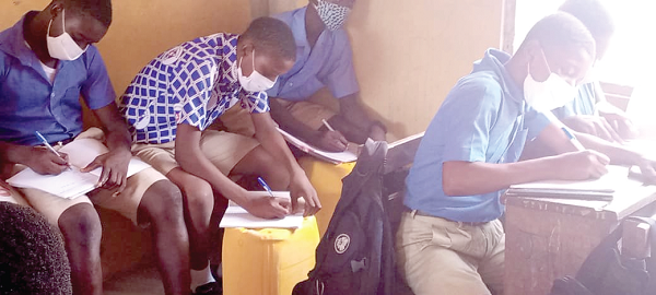 Some of the students of the Cape Coast Presbyterian Church School using gallons as tables to adhere to the social distancing protocol