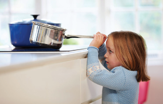 A child grabs the handle of a saupan on a stove