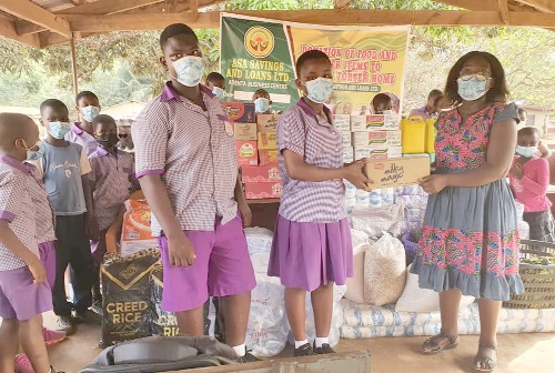 Joana Kensema Odei-Larbi (right), the Taifa Area Manager of Asa Savings and Loans Limited, handing over the items to one of the children in the Christ Faith Foster Home while other children looked on