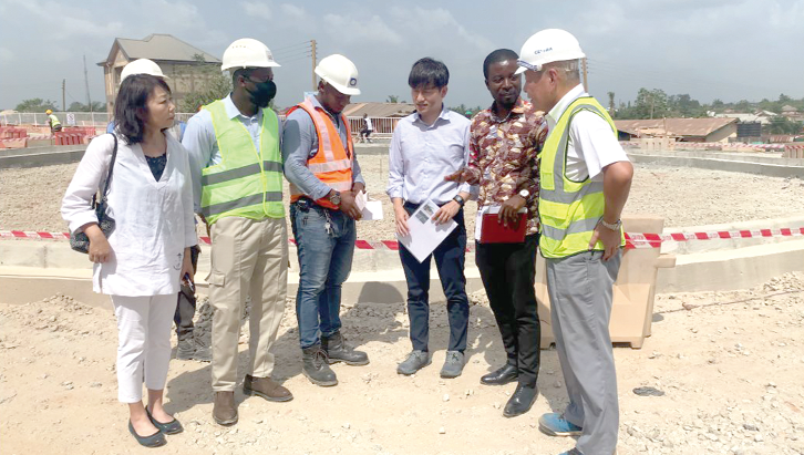 Shuji Soda (Right), Resident Supervisor for the project, having a conversation with Musah Ibrahim (2nd from right), the Coordinator for Development Cooperation,  whiles Katsumura Akihisa (3rd from right), the First Secretary for Development Cooperation,  Teragaki Yuriya (left), First Secretary for Public Relations and Culture, and other engineers engage.  INSET: An excavator working on the site 