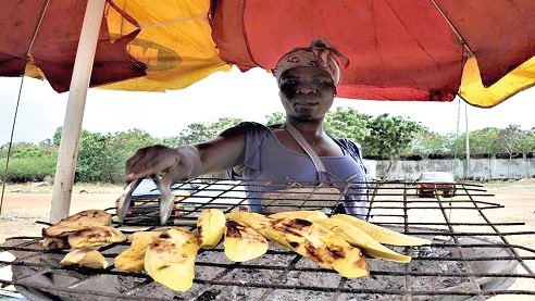 A woman roasting plantain (Kofi Brookman) by the roadside