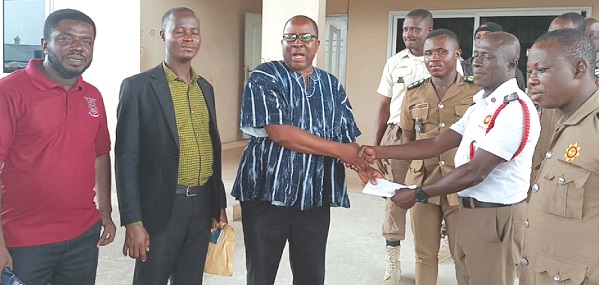 Francis Essel-Okyeahene (3rd from left), Chief Executive Officer of the Young Executive School, presenting the money to Gregory Joseph Martin (2nd from right), Assistant Division Officer in charge of Fire Safety of the GNFS. Looking on are some staff members of the school and the Awutu Senya East Municipal Fire Station