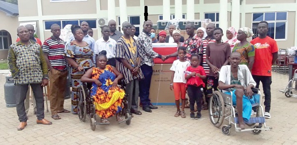 Mr Seth Asante (arrowed), District Chief Executive for Atiwa West, presenting one of the kits to a beneficiary, Mr Joseph Appiah from Sankubenase. With them are other beneficiaries, officials of the Social Welfare Department and the assembly.