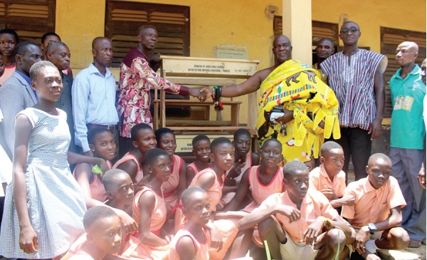 Nana Kwesi Addo II (right), Gyasehene of Pankese presenting the desks to Mr Peter Kwaku Ofori (left), head teacher of the Pankese DA Junior High School, while other staff and pupils of the school look on