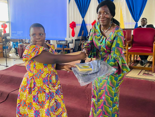 Mrs Della Sowah presenting a bag and a reading book to a student at the event