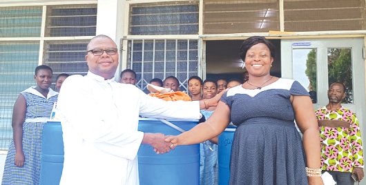 •Rev. Fr Delase Parku of the Sacred Heart Parish in Accra in a handshake with Benedicta Agbezudor, Headmistress of OLA SHS, after presenting the items to her on behalf of Abrokwah. Behind them are students of the school