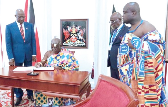 Otumfuo Osei Tutu II signing the visitor’s book. With him is Prime Minister Keith Rowley (left) and some officials from the Manhyia Palace