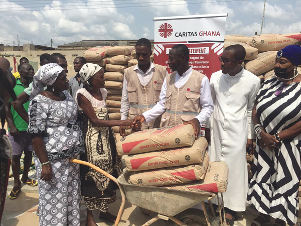 Rev. Father Amoah-Gyasi (3rd from right) presenting some bags of cement to Maame Abena Ampomah, a resident of Abii