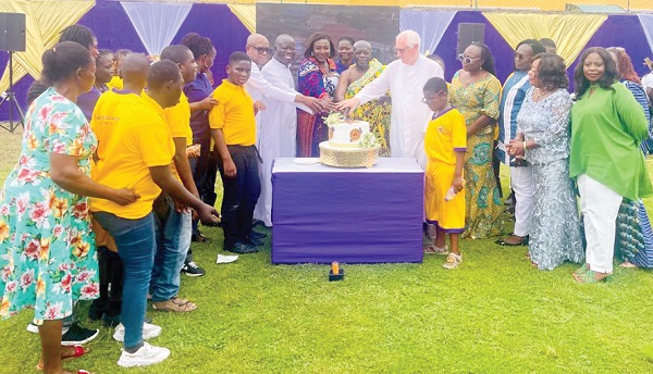  Nana Prah Agyensaim VI (arrowed) with Cornelia Boateng, Father Campbell, guests and children with autism cutting the anniversary cake