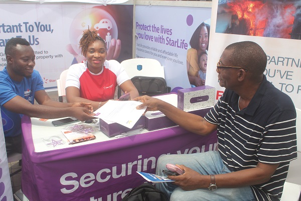 Sandra Osei-Abankwa (2nd from left), Manager, Underwriting and Client Relations of StarHealth, presenting an insurance policy to a customer at the fair.