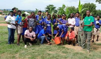 Nelson Asumani (squating 2nd from left) Headmaster of Ogome Anglican JHS planting a coconut seedling while Charity Adamnor Okrah holding a watering can watering the planted  seedling. Standing at the back are staff of ASA Savings and Loans and officials from the Somanya District Office of the Forestry Services Division including students.