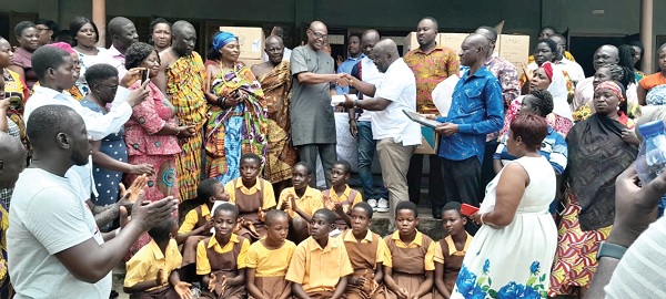Michael Okyere Baafi (in white polo shirt), MP for New Juaben South, presenting one of the tablets to Mustapha Haruna, New Juaben South Municipal Education Director. Looking on are Nana Kwasi Adinkra Kosopre (arrowed), Mawerehene of Nyamekrom, and other dignitaries. Seated in front are some of the beneficiary pupils