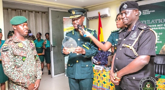 Kwame Asuah Takyi, the Comptroller-General of Immigration, reading the inscription on the memento before presenting it to newly-promoted AICO I Nurideen Abdul-Ganiew Takra (left). Looking on is COP Francis Ebenezer Doku, the Director-General of MTTD 