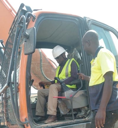 Akwannuasah Gyimah (left), MCE for Asokwa, operating the earth moving machine  to perform the sod cutting event for the road project at Ahinsan