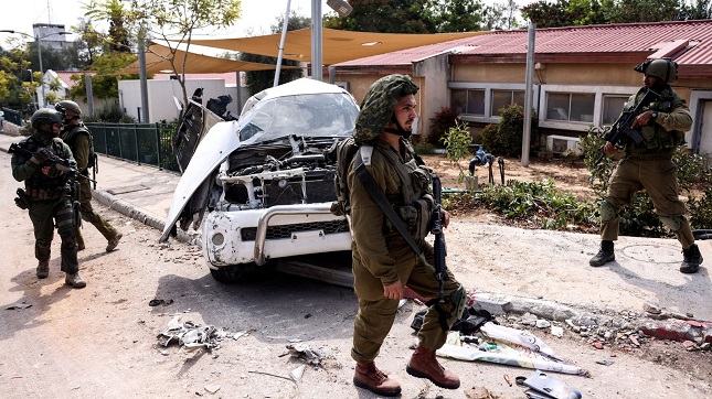 Israeli soldiers walk past a damaged car in Kibbutz Kfar Aza, in southern Israel