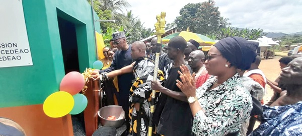 Nana Ansah Sasraku (arrowed), Chief of Potrase, being assisted by Ambassador Baba Gana Wakil (left), Resident Representative of ECOWAS in Ghana, to cut the tape to officially inaugurate the new water facility at Potrase