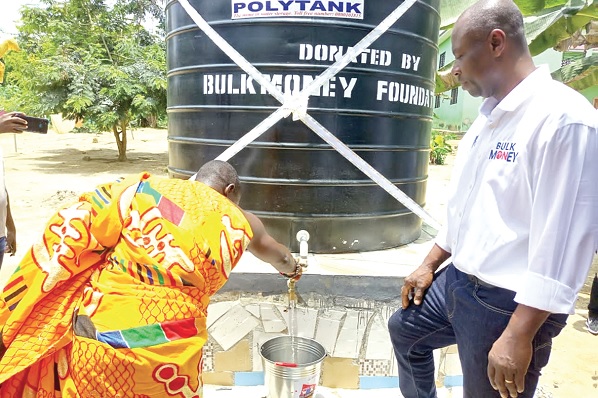 Nana Effah Amoama, the Krontihene of Akyem Aperade, drawing water from one of the boreholes to officially inaugurate the facilities. With him is George Niako (right), the CEO of Bulk Money Foundation