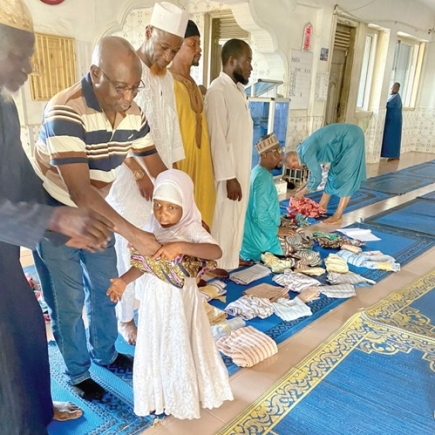 lbrahim Muhammed (2nd from left) presenting a set of dress to one of the orphans. Standing on his left in white attire is Nuhu Muhammed Abdalla, the Municipal Chief Imam